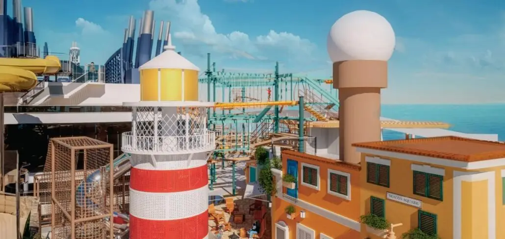 A colorful outdoor play area on MSC World America, featuring a red and white striped lighthouse, a tan tower with a white dome, ropes course structures, slides, and buildings with balconies against a blue sky and ocean backdrop.