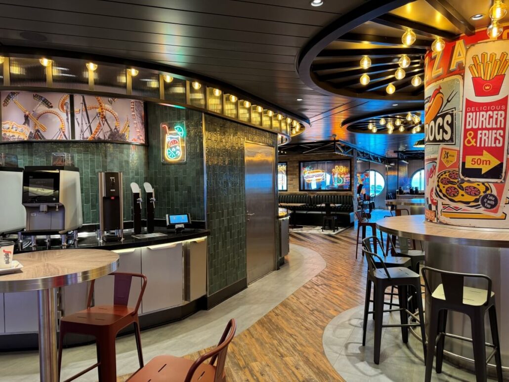 A modern, well-lit fast food restaurant interior aboard MSC World America features a drink dispenser, high chairs, neon signs, booth seating, and food-themed wall art—perfect for a casual family cruise dining experience. Wood and tile floors complete the look.