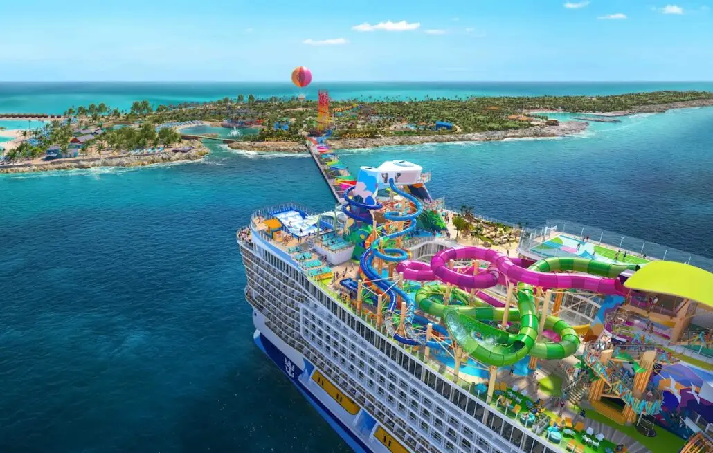 A large cruise ship with multiple colorful water slides is docked at an island with clear blue water, sandy beaches, palm trees, and a long pier leading to a distant hot air balloon.