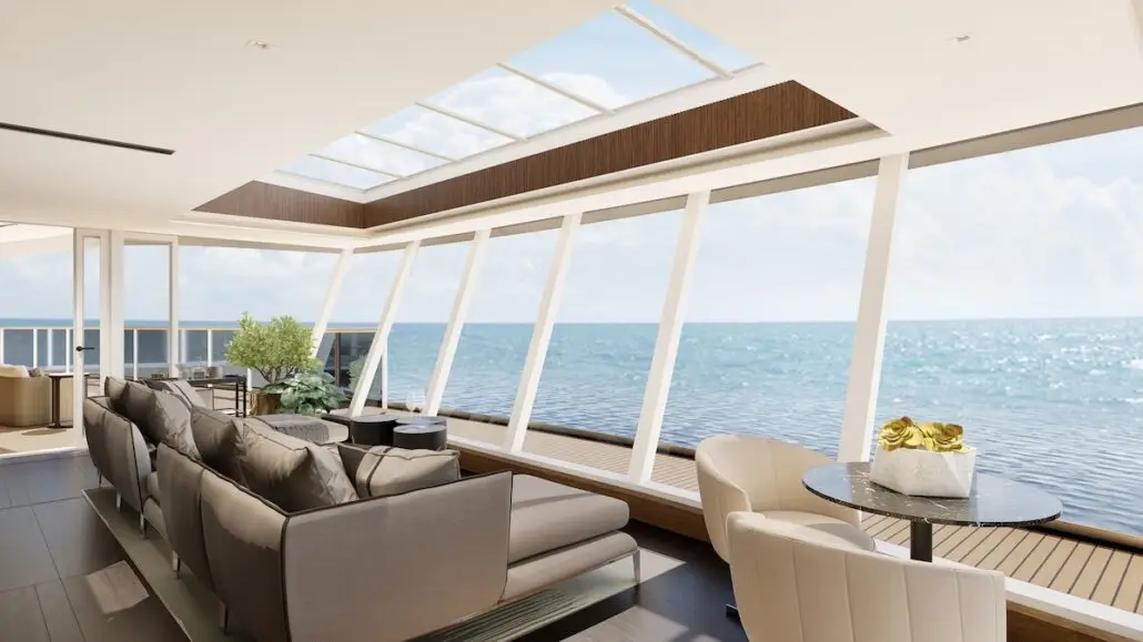 A modern yacht interior aboard the new Regent ship features large windows with an ocean view, a gray sectional sofa, armchairs, a small table with a gold centerpiece, and natural light streaming through the Skyview Suite's skylight.