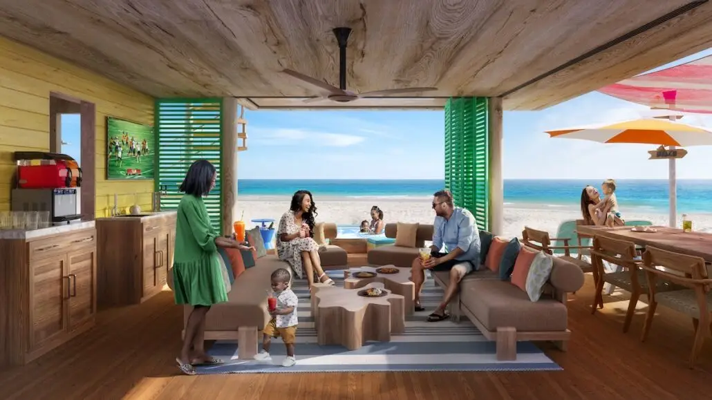 People relax in a beachfront cabana with wooden furniture, enjoying drinks and snacks. The scene includes adults and children, with the ocean and beach visible in the background on a sunny day.