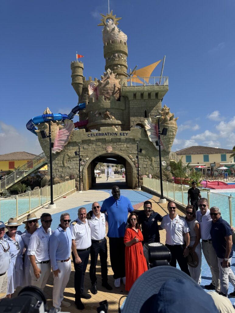 A group of people poses for a photo at the Grand Opening of Celebration Key, standing before a large sandcastle-themed entrance, with water slides and colorful structures visible in the background.