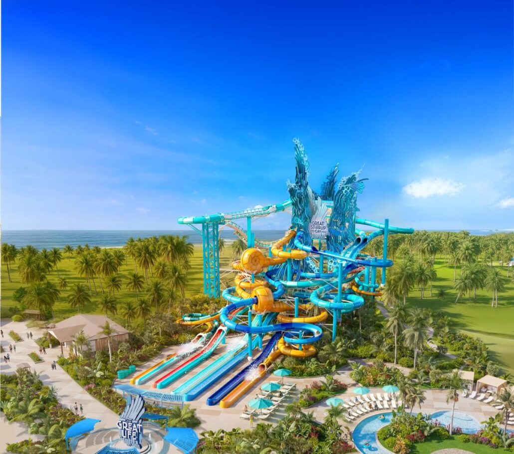 A large, colorful water slide structure with twisting tubes and multiple slides stands among palm trees and green lawns under a bright blue sky at the Norwegian Cruise Line’s Great Stirrup Cay water park.