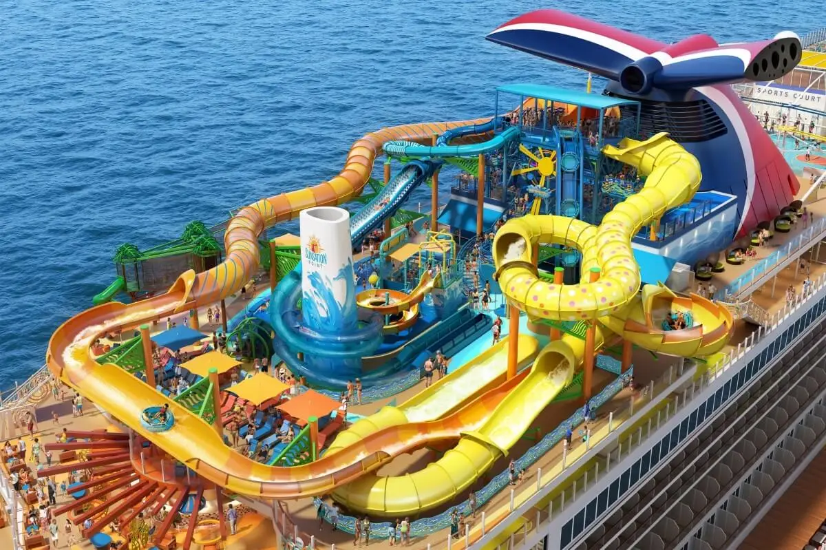 Aerial view of a Royal Caribbean cruise ship deck featuring large, colorful water slides, a splash zone, and various water play structures, surrounded by people and positioned on the ocean.