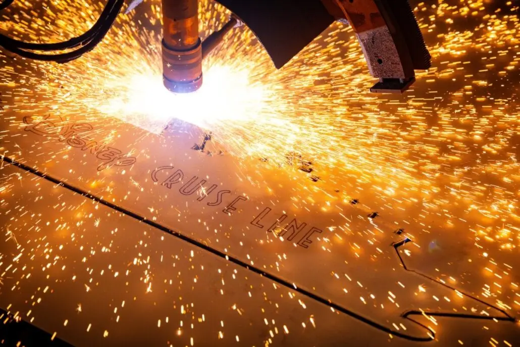 A close-up of a CNC laser cutting machine from Meyer Werft emitting bright sparks as it cuts through a metal sheet with the words “CRUISE LINE” visible on the surface, marking progress toward the Disney Destiny's November Launch.