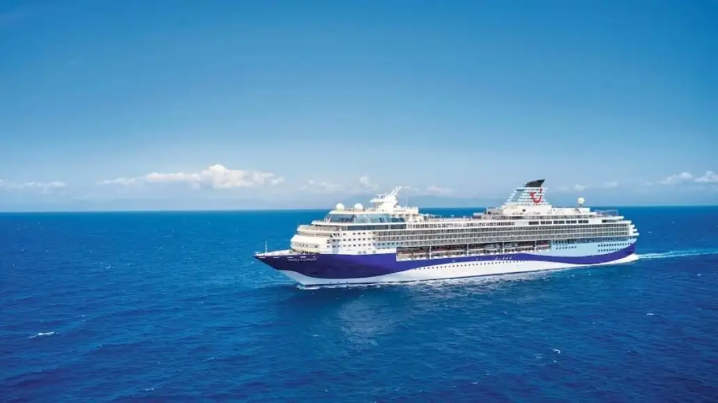 A large cruise ship with a sparkling pool sails across a calm blue ocean under a clear sky, offering serene views for every elderly guest on board.