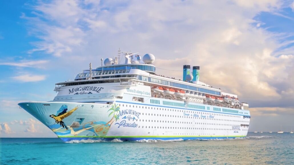 A large white cruise ship labeled "Margaritaville at Sea Paradise" sails on calm blue water under a partly cloudy sky, featuring tropical-themed artwork on its hull and promoted as an all-you-can-sail pass by the cruise line.