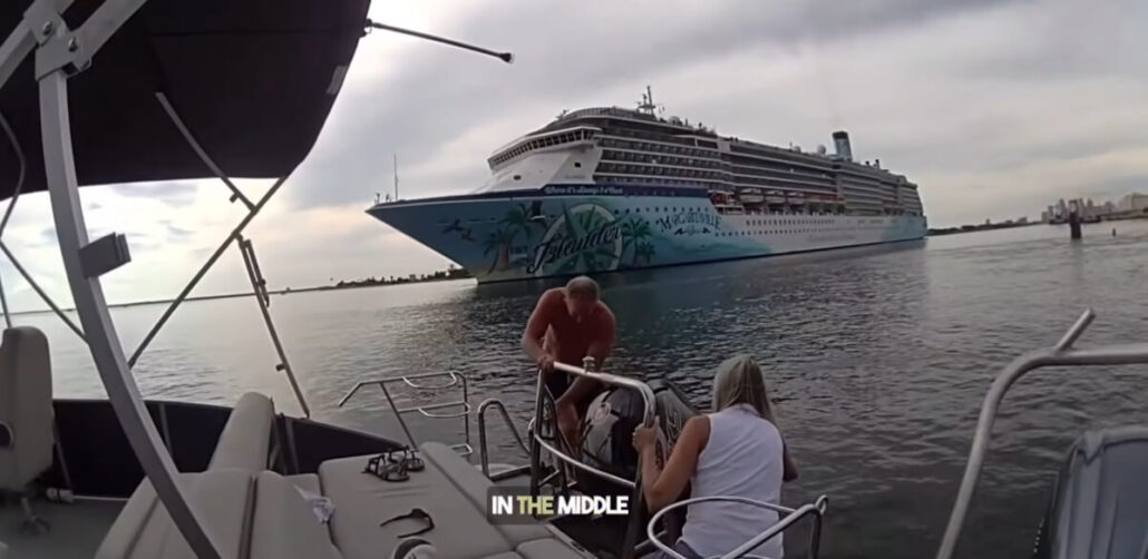 Two people on a disabled small boat appear to be tying or untangling ropes as a large cruise ship with tropical-themed artwork looms in the background. The text "IN THE MIDDLE" is visible at the bottom center of the image.
