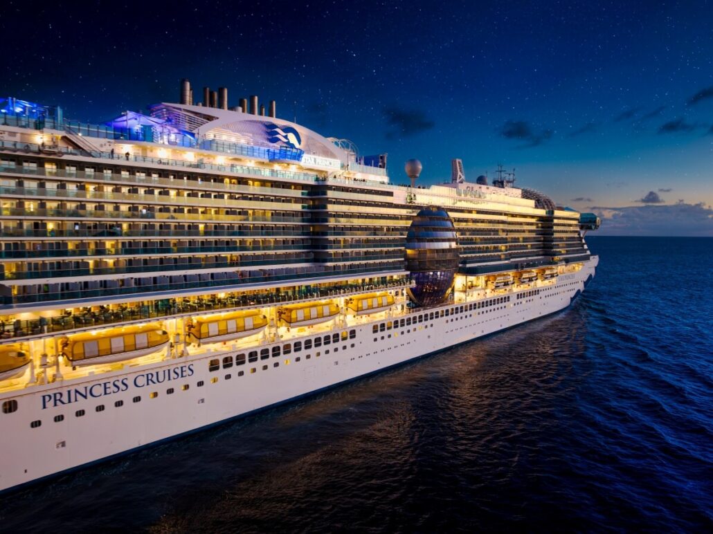 A large Star Princess ship from Princess Cruises is shown at night, illuminated with lights during Mediterranean Sailings, gliding on calm ocean water under a clear, starry sky.