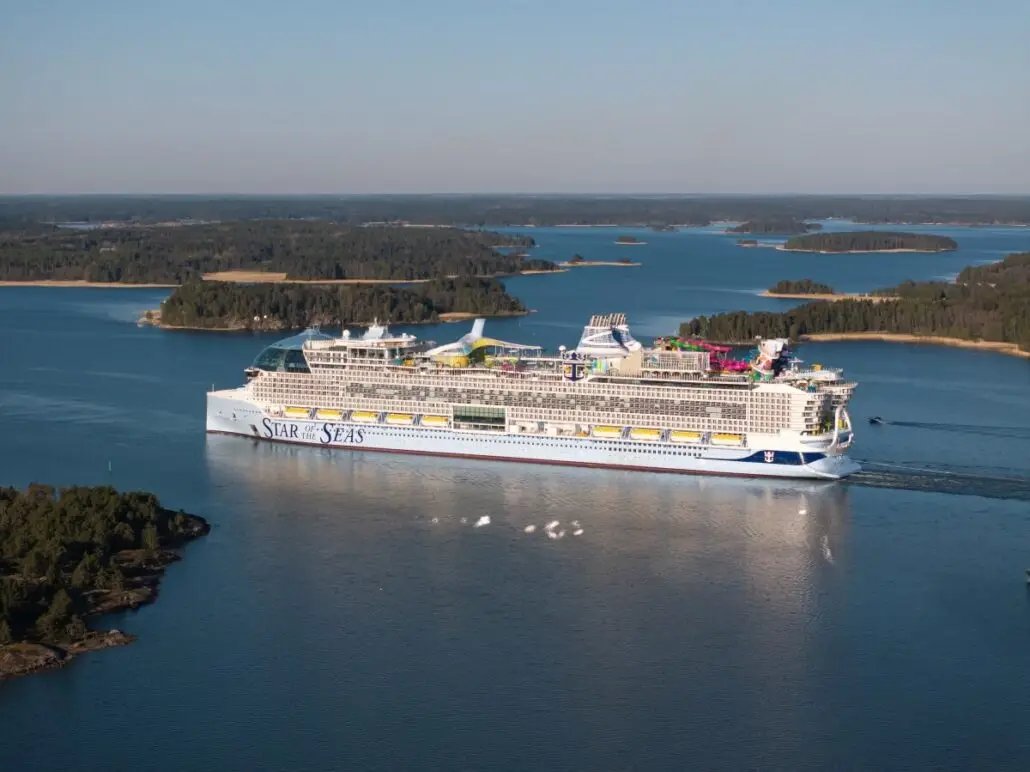 The "Star of the Seas," one of the bigger ships, sails through calm blue water past forested islands under a clear sky. With multiple decks and colorful structures, it's perfect for short cruises to beautiful destinations.