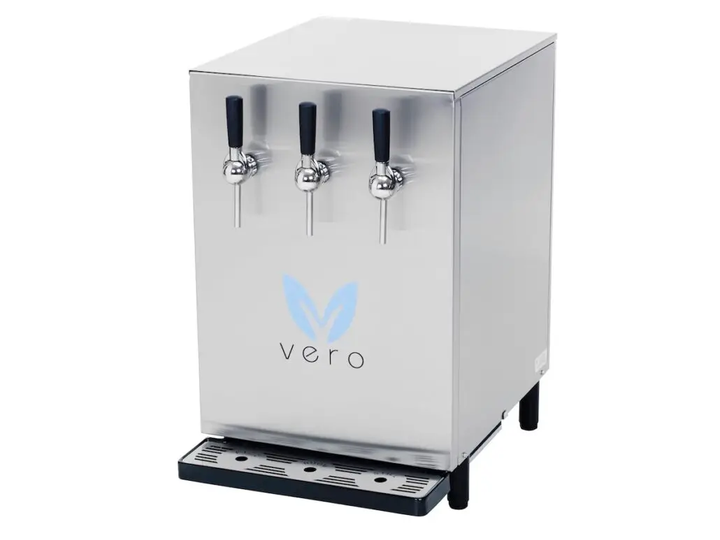 A stainless steel water dispenser with three black-handled spouts on the front, labeled "vero" with a blue leaf logo, stands on black legs and features a drip tray at the bottom—perfect for replacing bottled water on Norwegian Hawaii cruises.