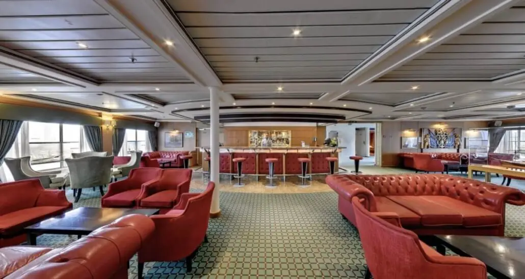 Spacious lounge area with red leather sofas, armchairs, a bar with stools, and large windows—ideal for relaxing on a cruise ship while staying informed about the CDC’s guidance on avoiding unsafe water.