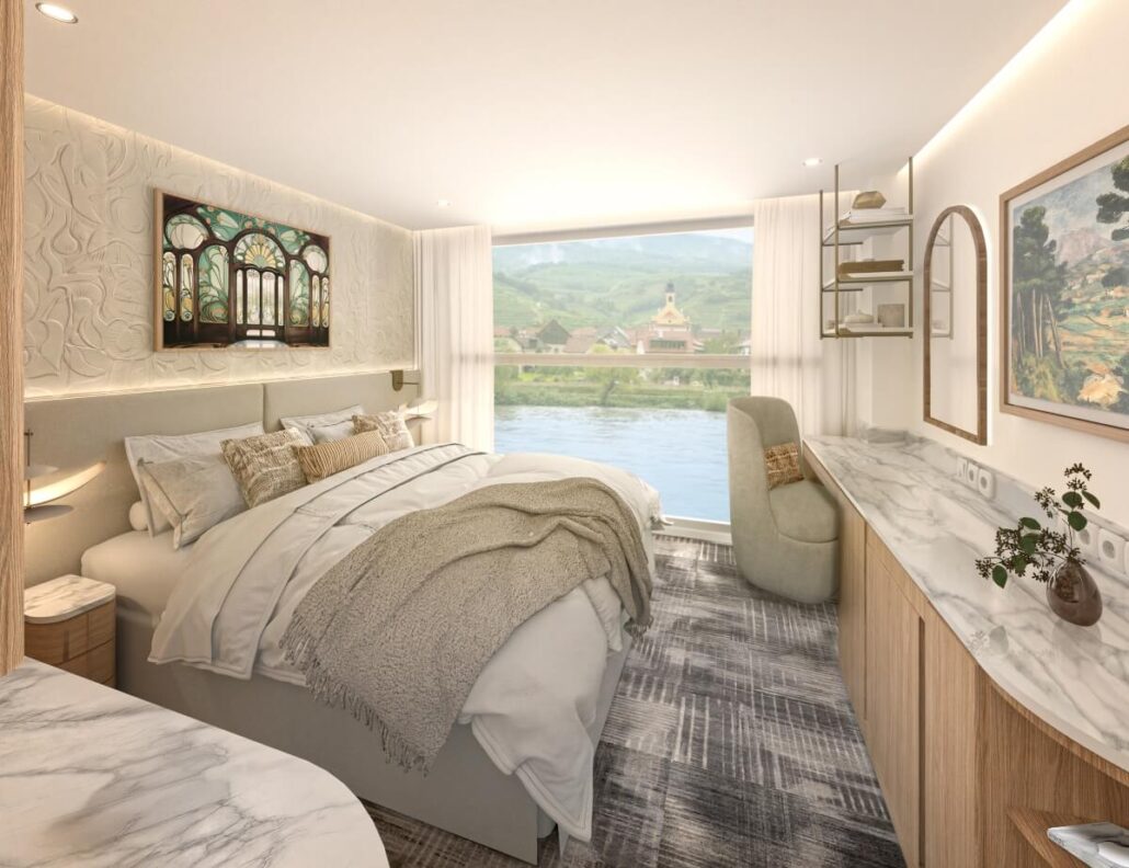 A cozy, modern bedroom with a large bed, neutral bedding, marble countertops, a desk and chair, wall art, and a large window—offering a Celebrity river cruise vibe with scenic views of the river and village nestled among rolling hills.