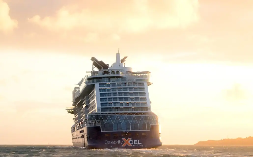 The Celebrity Xcel, fresh from sea trials, sails away from shore at sunset, its name shining as the sky glows orange and the water reflects the light ahead of its November Launch.
