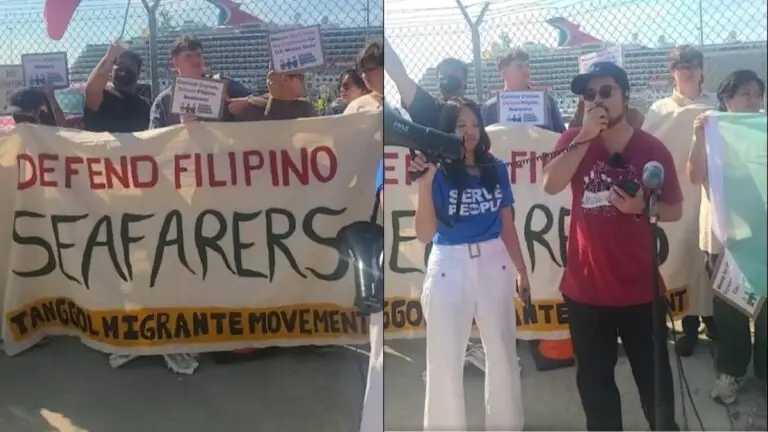 A group of people hold a banner reading "Defend Filipino Seafarers" at a protest for Filipino crew members. Two individuals stand in front, one speaking into a microphone, while others hold signs behind a chain-link fence.