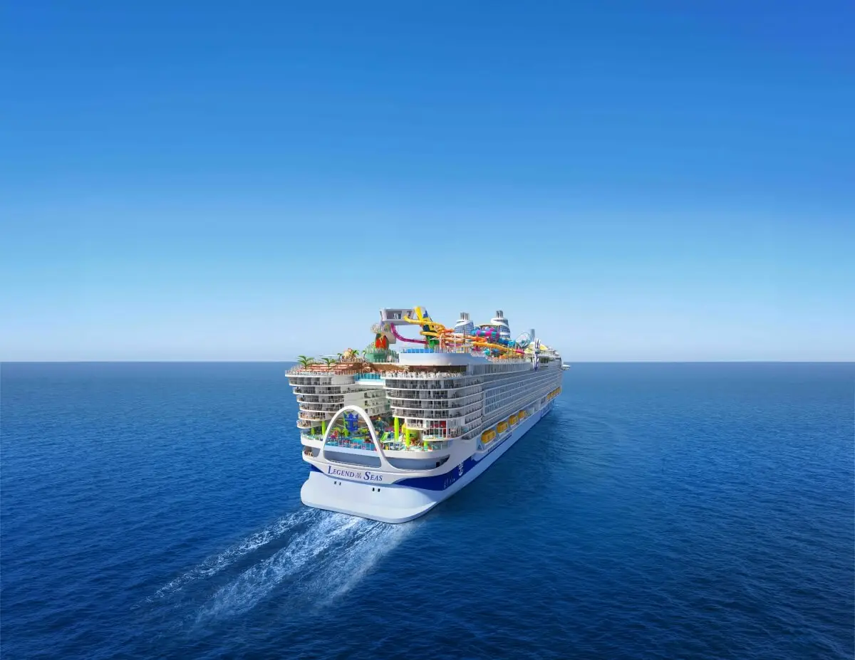 A large Royal Caribbean cruise ship named "Icon of the Seas" sails on calm blue ocean water under a clear sky, with colorful water slides, expanded dining options, and outdoor decks visible on the upper levels.