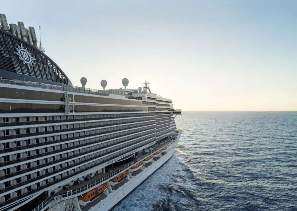 The MSC Seascape sails on calm blue ocean water under a clear sky near Galveston, with lifeboats visible along its side and the sun low on the horizon.