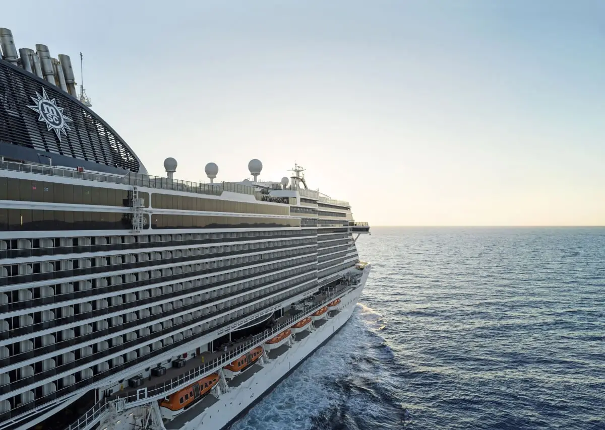 The MSC Seascape sails on calm blue ocean water under a clear sky near Galveston, with lifeboats visible along its side and the sun low on the horizon.