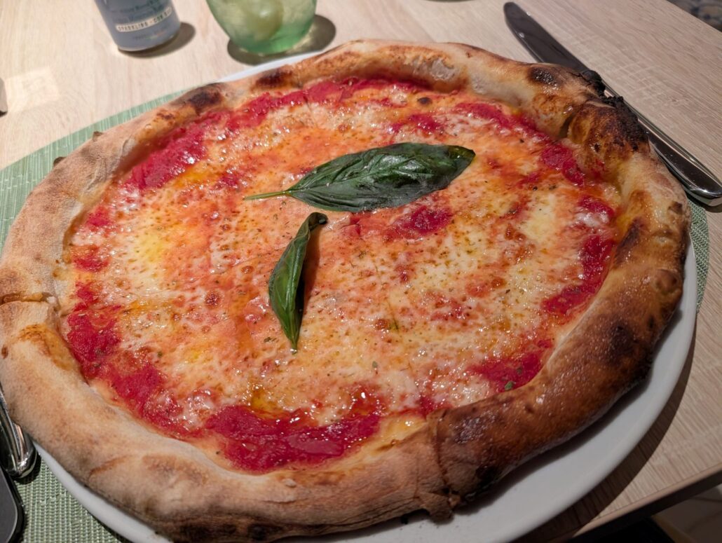 A classic Margherita pizza with tomato sauce, melted cheese, and basil leaves on top, served on a white plate on a wooden table—perfect for savoring during your inaugural cruise aboard the Star Princess.