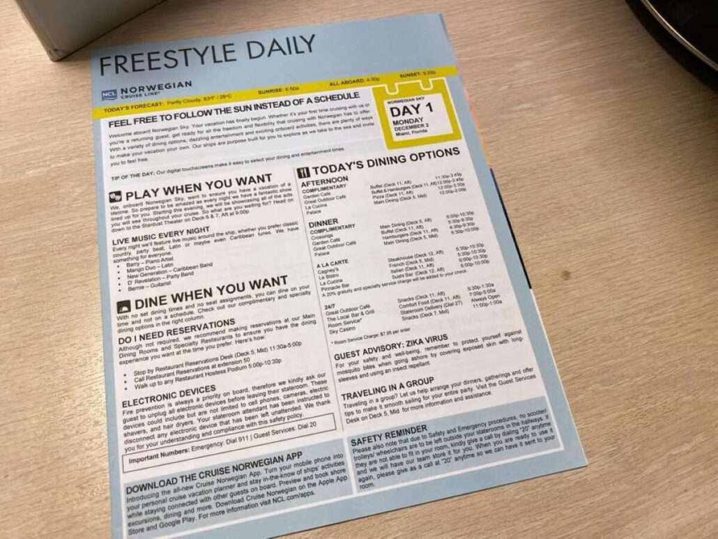 A Norwegian Cruise Line daily newsletter sits on a wooden surface. The page lists activities, dining options, reminders, and safety info for Day 1, Monday. Part of a round black and white object is visible near the staterooms directory.