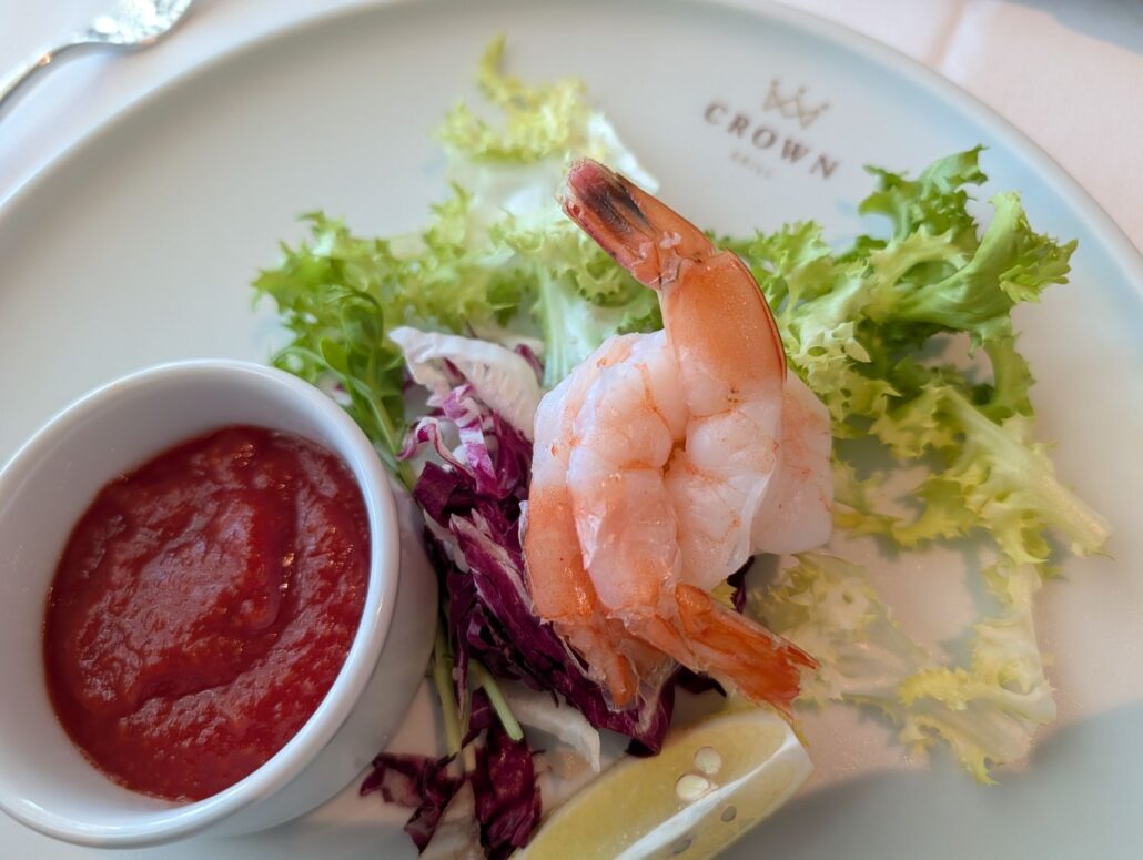 A plate from the Star Princess dining room features two shrimp on mixed greens, a lemon wedge, and cocktail sauce. The "CROWN" logo adds a touch of elegance—a tasty highlight for any trip report.