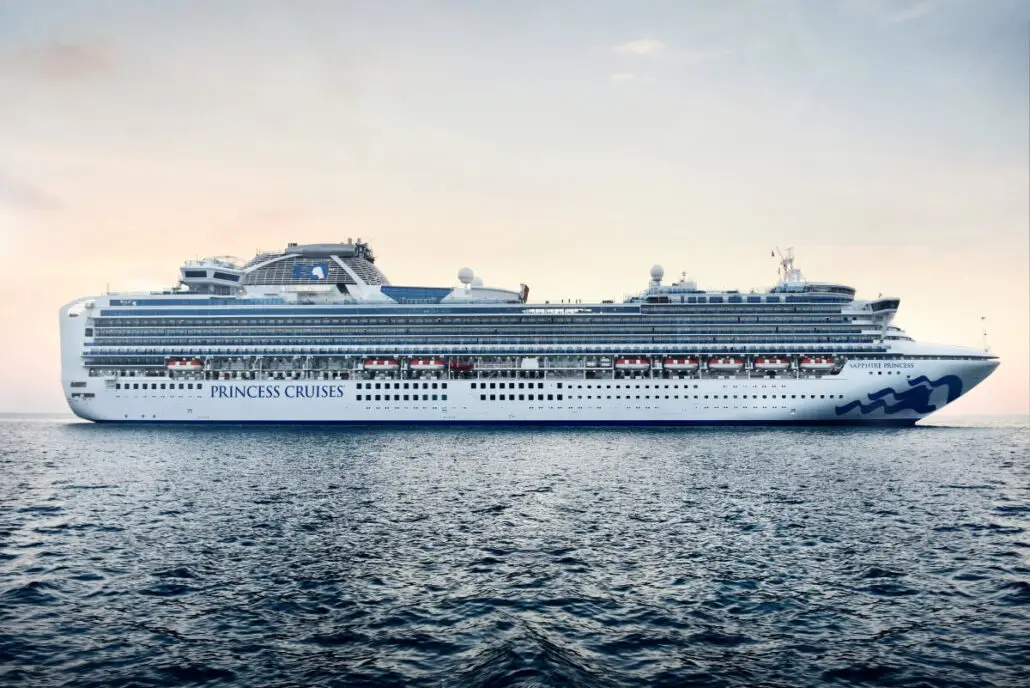 The Sapphire Princess, fresh from drydock, sails on calm water under a light sky, with multiple decks, balconies, and luxurious specialty dining options visible along the side.