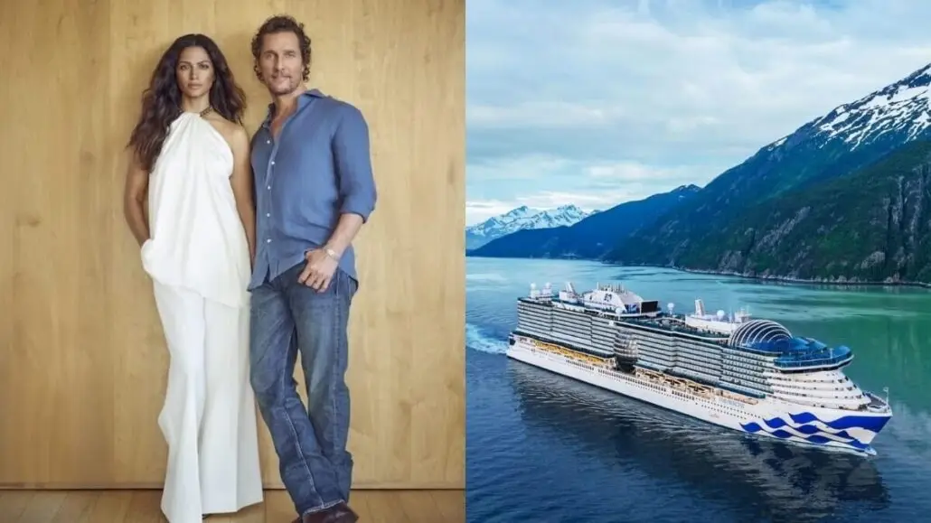 A woman in a white outfit and a man in a blue shirt and jeans, looking like godparents, stand against a wooden wall. Next to them, a Princess Cruise Ship sails on turquoise water surrounded by mountains.