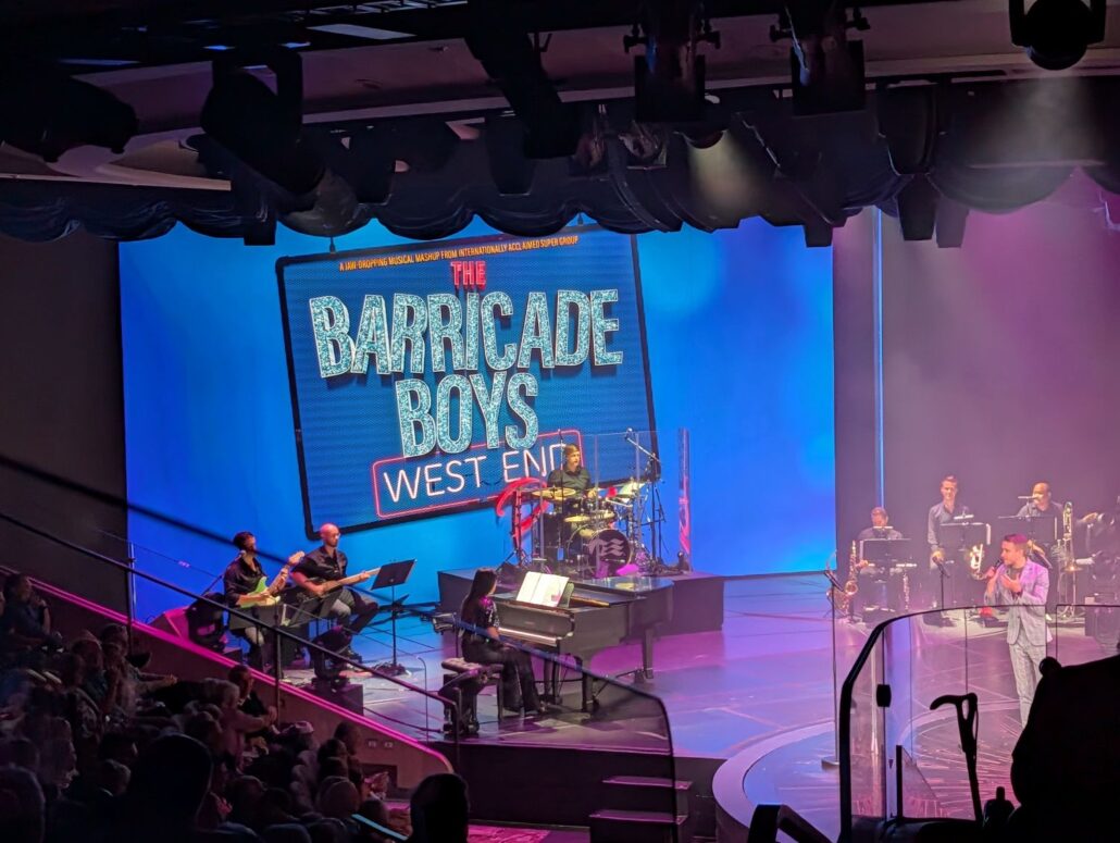 A stage on the Star Princess comes alive as musicians and a singer perform before a large screen reading “The Barricade Boys West End.” The brightly lit scene delights guests on this unforgettable inaugural cruise.