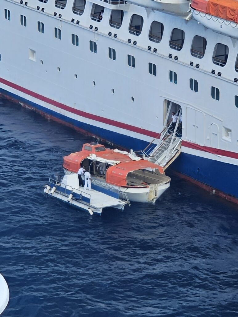 A lifeboat and a small boat are positioned next to a large Carnival Ship in Cozumel. Two people in white uniforms are on the boats, and another person is entering the ship through a side door above the waterline.