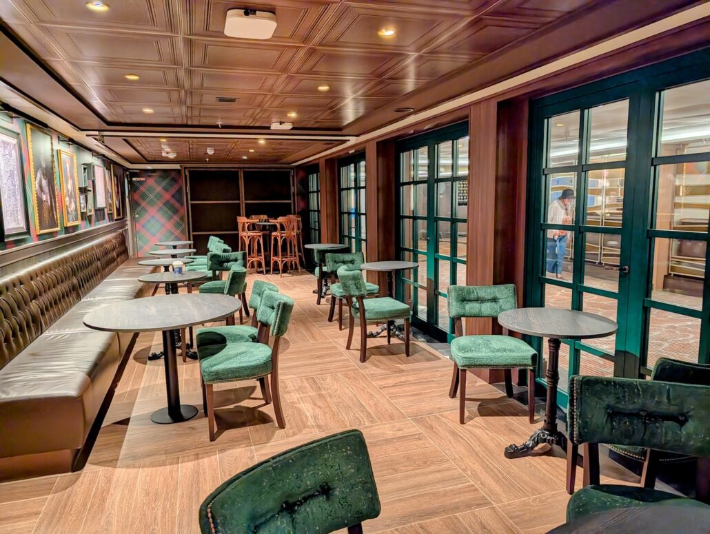 A modern lounge with green upholstered chairs, round tables, and a long cushioned bench along one wall. Framed artwork is displayed on the left. Perfect for enjoying nightly entertainment after exploring Princess Cay, with wood-paneled ceilings and floor-to-ceiling windows.