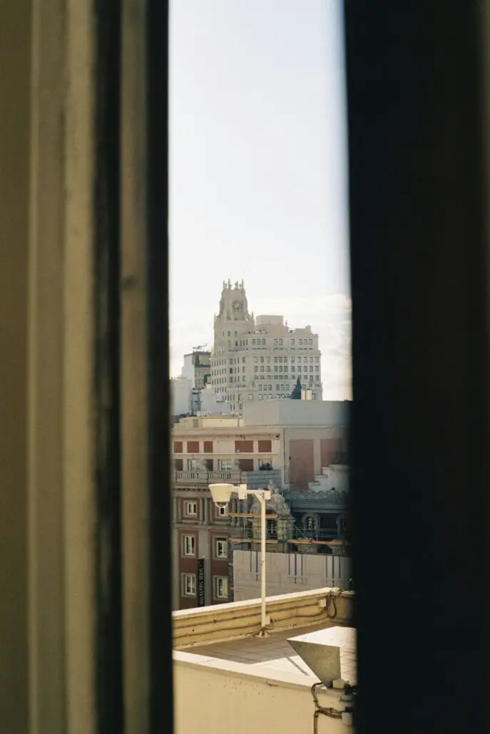 A cityscape in Spain is seen through a narrow gap between two blurred surfaces, with a tall, ornate white building in the background—ideal inspiration for first-time visitors Spain seeking hidden views and travel tips.