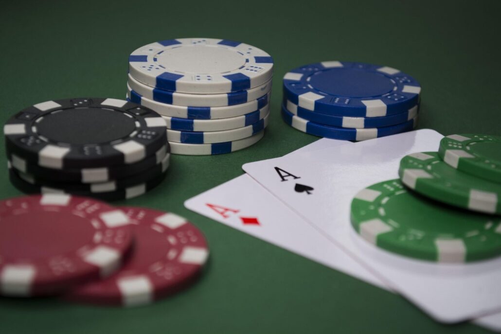 Poker chips in different colors are stacked on a green table next to two playing cards, an ace of spades and an ace of diamonds, with green chips placed on top—perfect for showcasing Casino Operations in a Cruise Ship Casino setting.