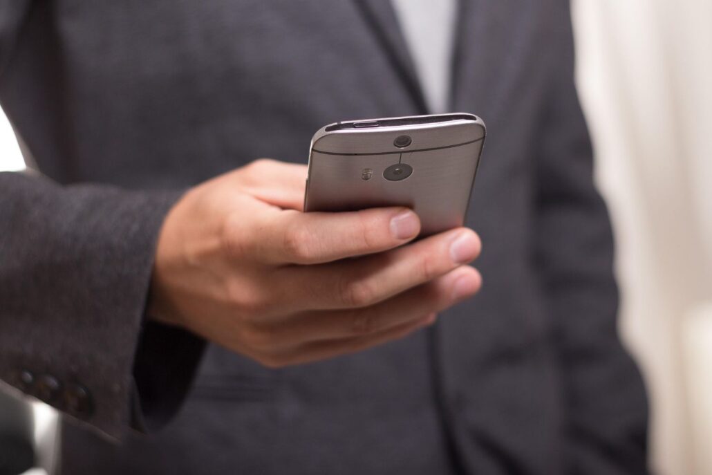 A person wearing a suit holds a smartphone in their right hand, with the phone's back facing the camera. The blurred background suggests they're ready to capture essential Spain travel tips for first-time visitors to Spain.