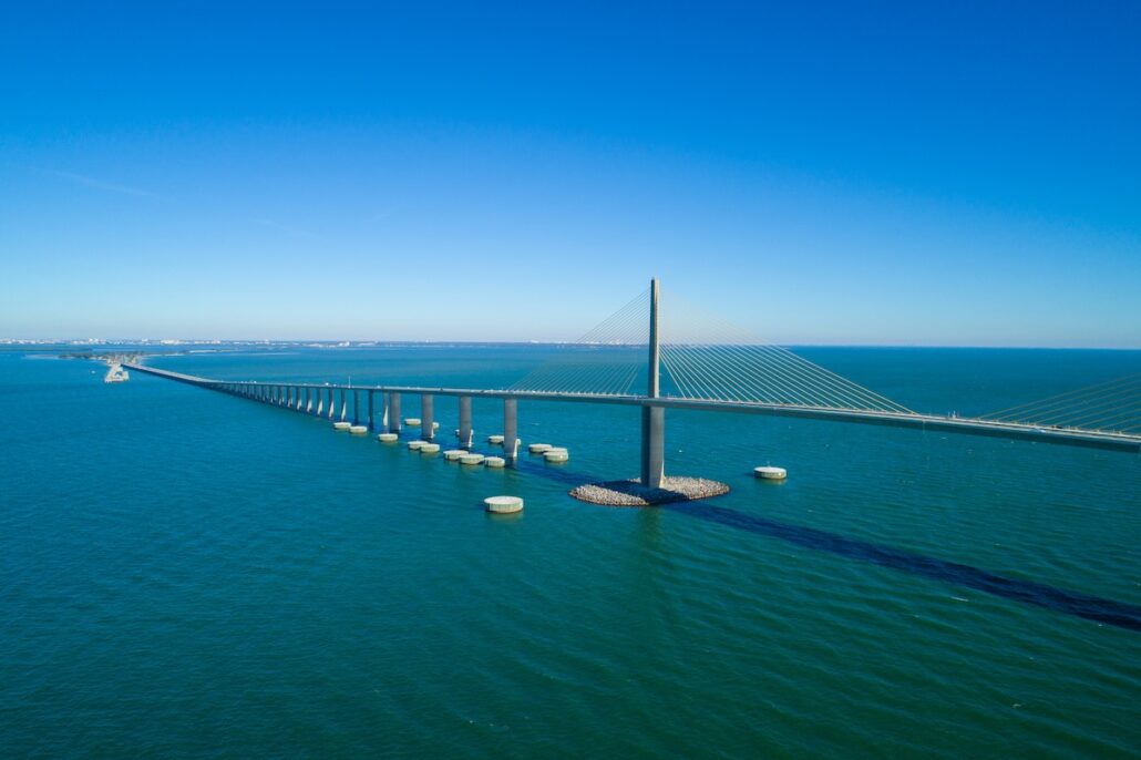 A long cable-stayed bridge with multiple support pillars extends over Tampa Bay’s blue waters under a clear sky, connecting two distant land masses—a vital link considered in the latest Port Proposal for mega cruise ships.