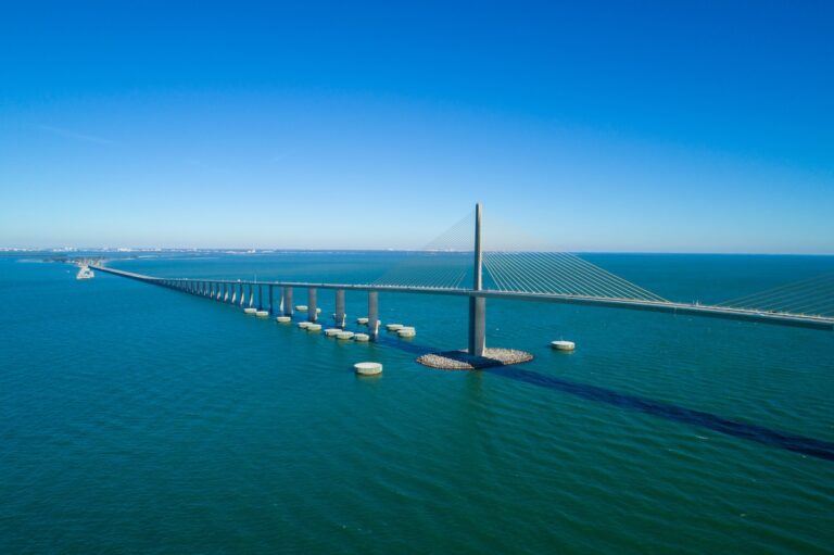 A long cable-stayed bridge with multiple support pillars extends over Tampa Bay’s blue waters under a clear sky, connecting two distant land masses—a vital link considered in the latest Port Proposal for mega cruise ships.