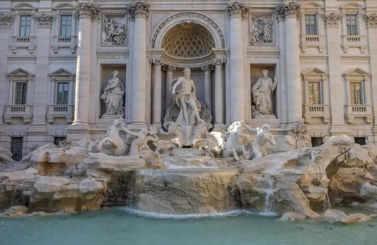 The Trevi Fountain in Rome, Italy, features a large central statue of Oceanus flanked by two smaller statues, ornate architectural details, and water flowing into a clear pool—no entrance fee is required to enjoy this iconic landmark.