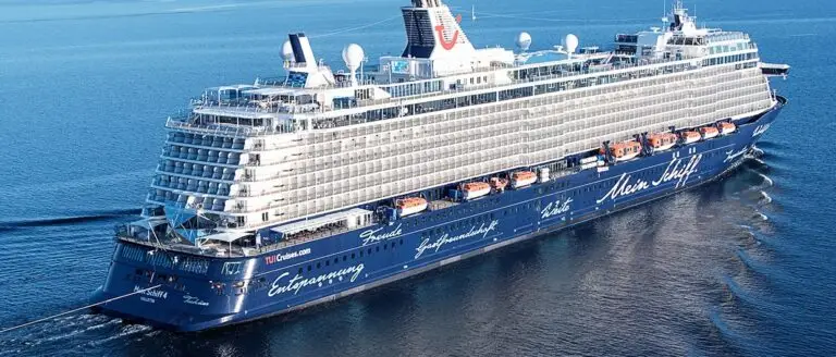 A large, modern cruise ship sails on calm blue water. The ship has multiple decks, balconies, and lifeboats along the sides. Despite its tranquility, a sudden panic aboard spreads rumors of a missile Abu Dhabi near the horizon.