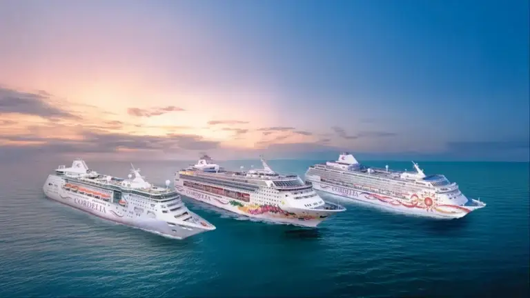 Three large cruise ships, including the Norwegian Sky, are sailing side by side on calm blue ocean water under a pastel-colored sky at sunset.