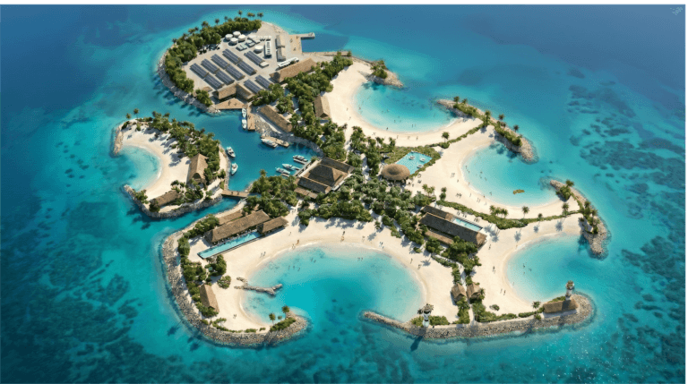 Aerial view of a small, palm-lined island with sandy beaches, turquoise water, several modern buildings, swimming pools, and docks; surrounded by clear blue ocean.