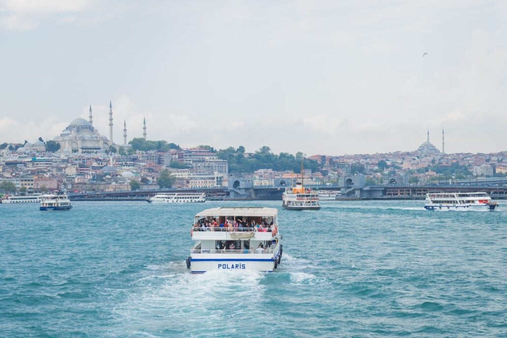 A white passenger ferry named POLARIS travels on a blue waterway near the Bosphorus Yacht, with several other boats nearby; a cityscape with historic buildings and mosques with minarets rises in the background.