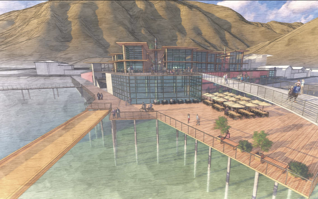 A modern waterfront building with large glass windows and outdoor seating is situated on a pier over water, surrounded by wooden walkways. Mountains rise in the background under a partly cloudy sky. People are walking on the pier.