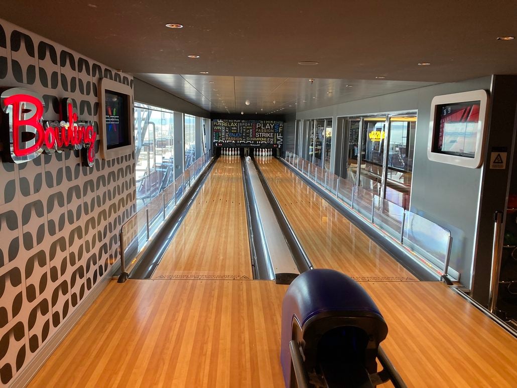 A bowling lane with pins set at the end, viewed from behind the ball return on a cruise ship where passengers might discuss cruise compensation.