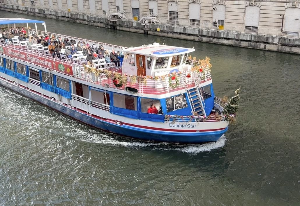 The Shoreline Sightseeing boat “Evening Star” carries passengers along a city river on a Chicago architecture tour, the vessel decorated with holiday garlands.