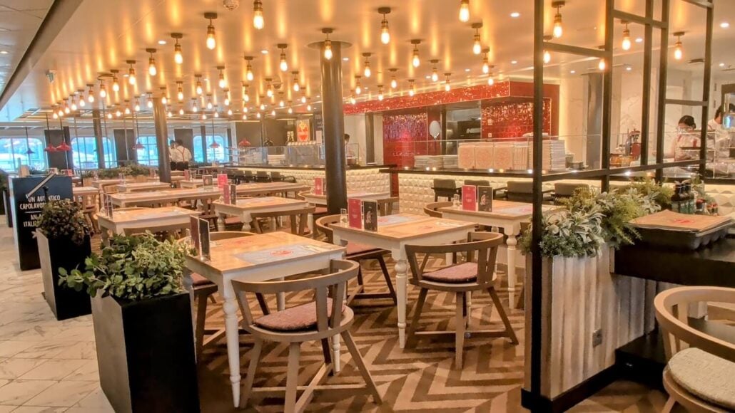 Dining room in a restaurant with rows of white tables, wooden chairs, and numerous pendant lights hanging from the ceiling.