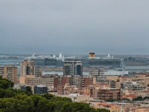 A Costa Toscana cruise ship with a yellow funnel docked behind a dense urban cityscape.