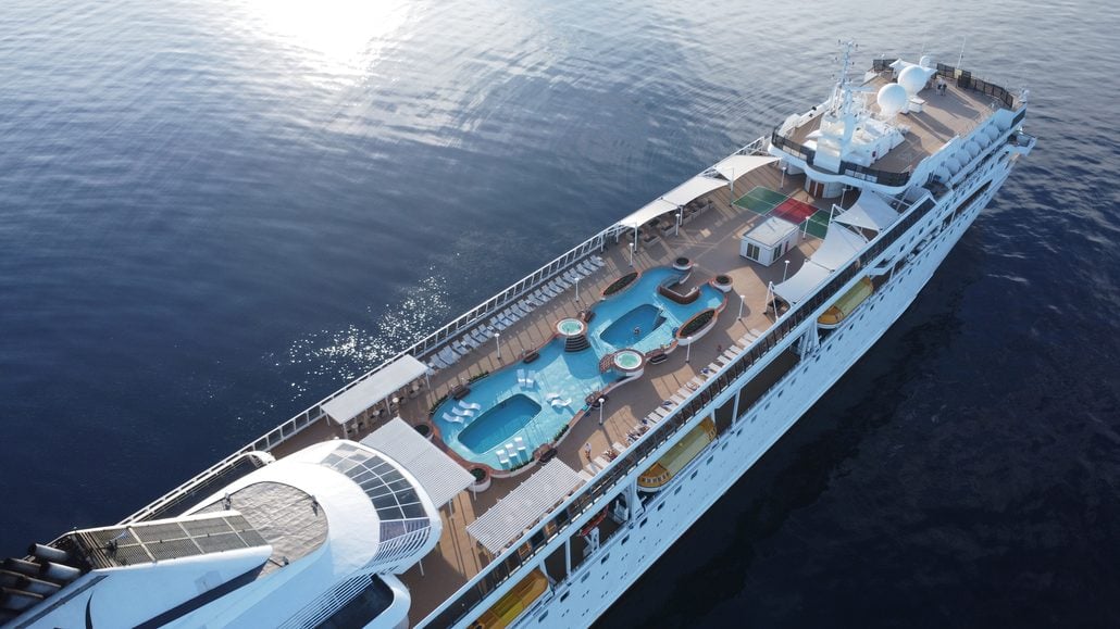 Aerial view of a cruise ship deck featuring two swimming pools and several whirlpools surrounded by lounge chairs, capturing the essence of cruise lifestyle.