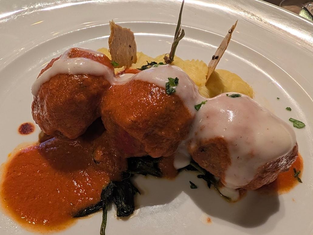 Three large meatballs covered in red and white sauce, served over a bed of greens and mashed potatoes at Costa Toscana.