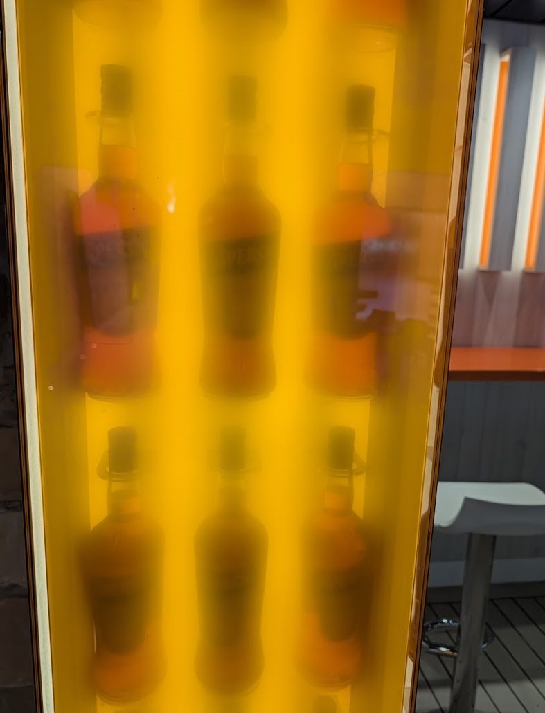 Six amber-colored Costa Toscana liquor bottles arranged in two rows inside a backlit, orange-toned display case.