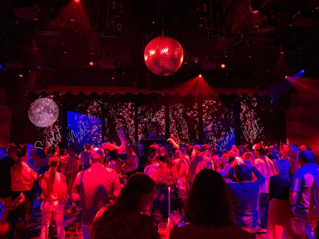 A crowd dances at a Scarlet Night party under a disco ball in a dark, red-lit venue that serves as a reminder for passengers to be aware of their travel rights.