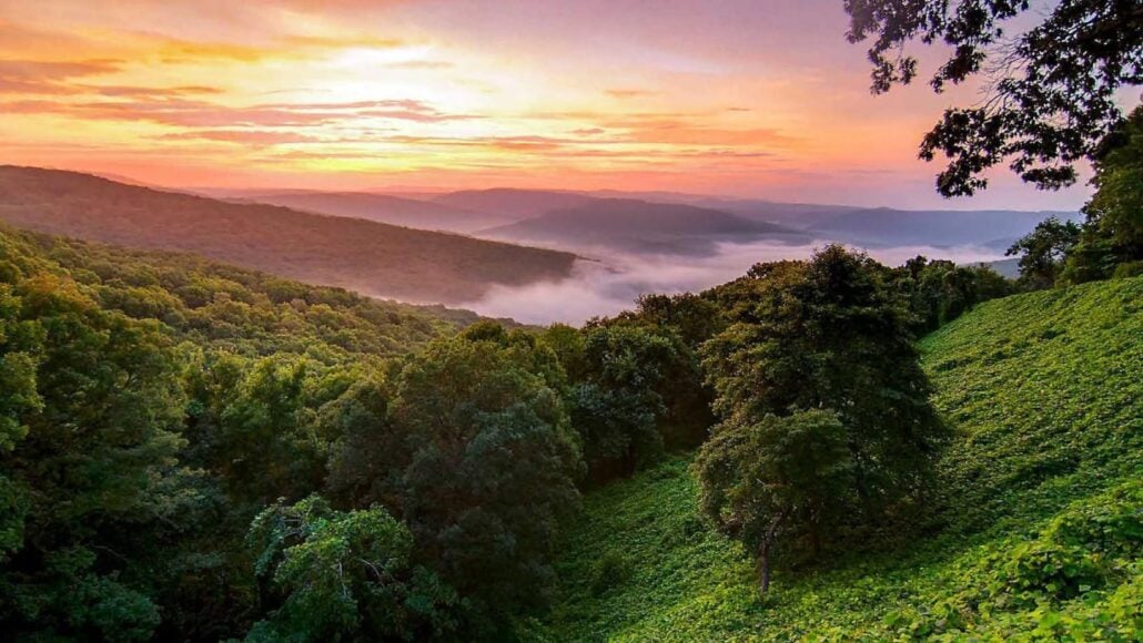 A valley of forested hills covered in morning fog beneath a sunset sky, perfect for your next Branson vacation.